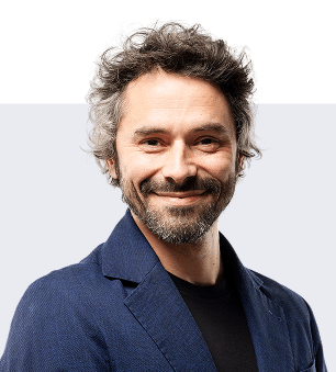 Uomo sorridente con capelli castani e brizzolati, barba e giacca blu